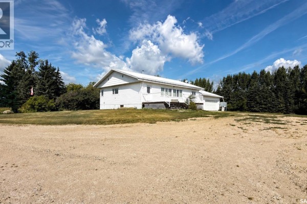 Exterior view of a white farm house with a deck and attached garage, surrounded by green grass and trees. - Rm Of Kellross Farm, Kellross Rm No  247