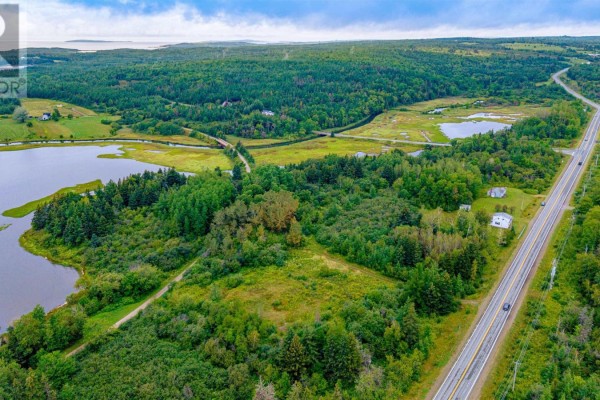 Aerial view of a rural landscape with water, trees, a highway, and houses. - Route 19, Judique North