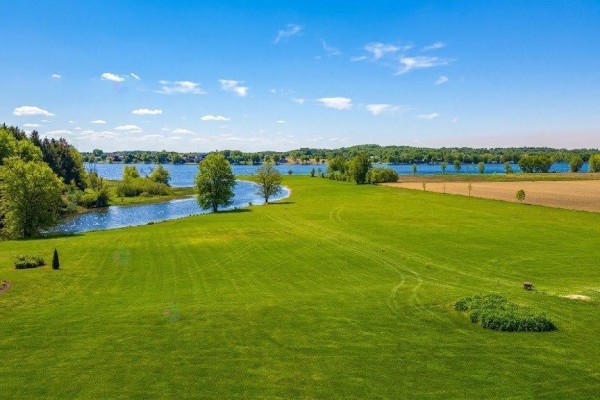 Expansive green lawn with a winding waterway and distant lake under a bright blue sky. - Rue Notre-dame, Montebello