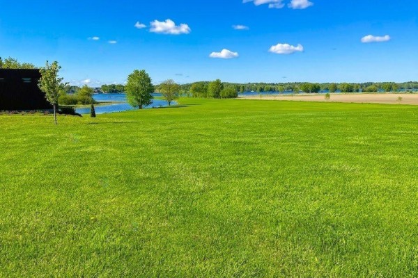 Wide open green field with scattered trees and a view of a calm body of water. - Rue Notre-dame, Montebello
