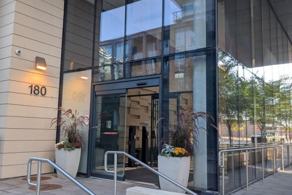 Entrance to a modern condo building with automatic glass doors and planters. - S104 - 180 Mill Street, Toronto