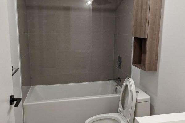 A bathroom with a bathtub, toilet, and grey tiled walls. - S104 - 180 Mill Street, Toronto