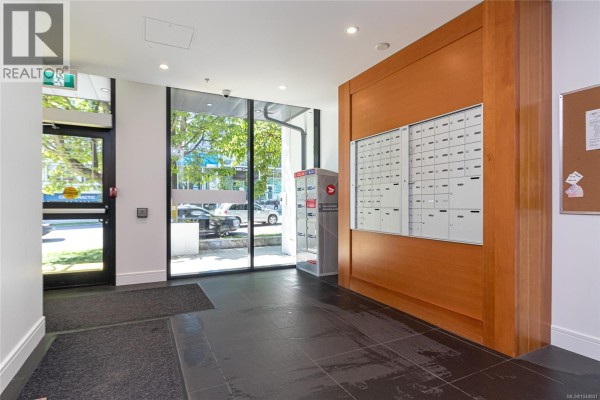 Apartment building lobby with mailboxes, glass doors, and dark tile flooring. - S404 1411 Cook St, Victoria