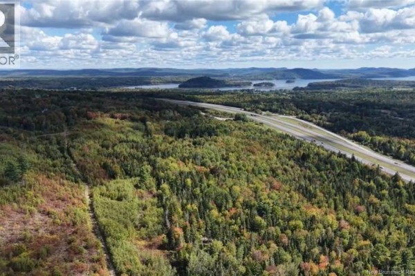 Aerial view of a highway running alongside a vast expanse of mixed forest with distant lakes under a cloudy sky. - Saint David Ridge Road, Oak Bay