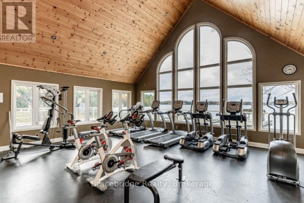 Home gym with treadmills, stationary bikes, elliptical, and large arched windows. - Sandfield 3 W3 - 3876 Muskoka Rd 118 Highway W, Muskoka Lakes