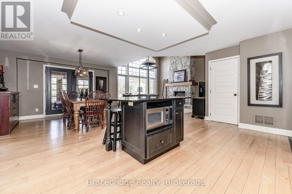 Open concept kitchen and dining area with island, stone fireplace, and dining table. - Sandfield 3 W3 - 3876 Muskoka Rd 118 Highway W, Muskoka Lakes