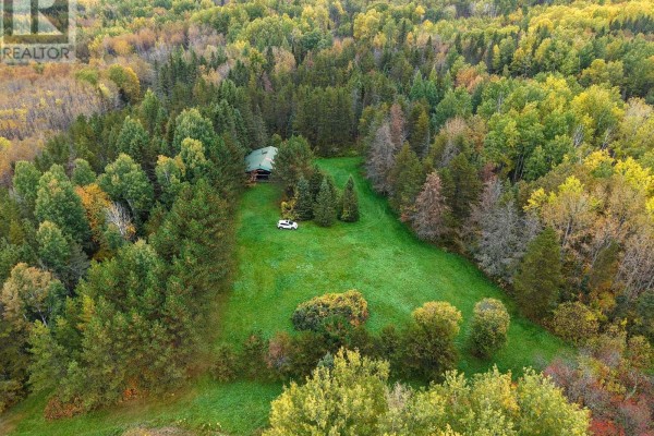 Aerial view of a log cabin property featuring a treed lot and a bright green grassy clearing. - Shalf Lt 6 Con 2 Day Mar Road, Englehart