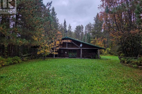 Front view of a rustic log cabin with a green metal roof, set in a cleared grassy area surrounded by trees. - Shalf Lt 6 Con 2 Day Mar Road, Englehart