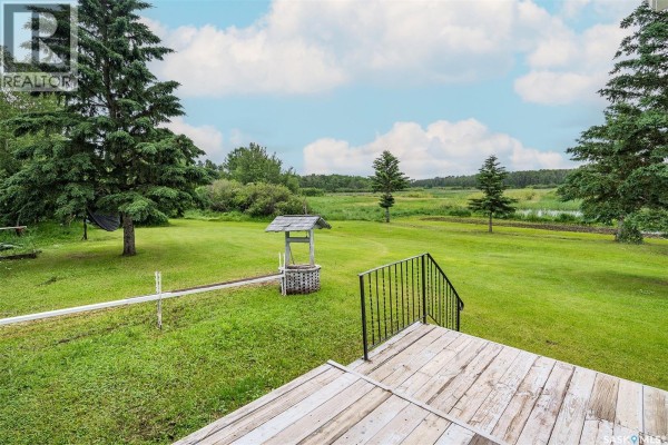 View of a wooden deck with railing overlooking a grassy field with a well and trees. - Sherman, Big Quill Rm No  308