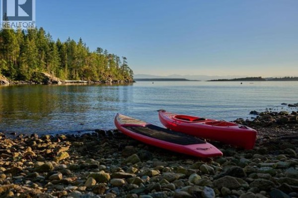 Two red kayaks and a paddleboard rest on a rocky shore with calm water and treed hills. - Sl 18 Sarah Point Road, Powell River
