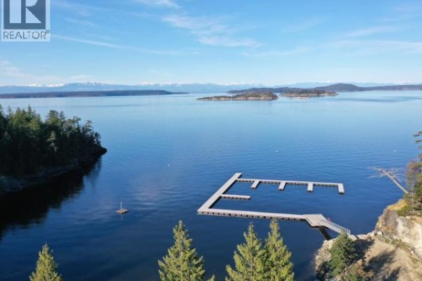 An aerial view of a marina with docks in a wide bay surrounded by forested land and distant mountains. - Sl 28 Sarah Point Road, Powell River