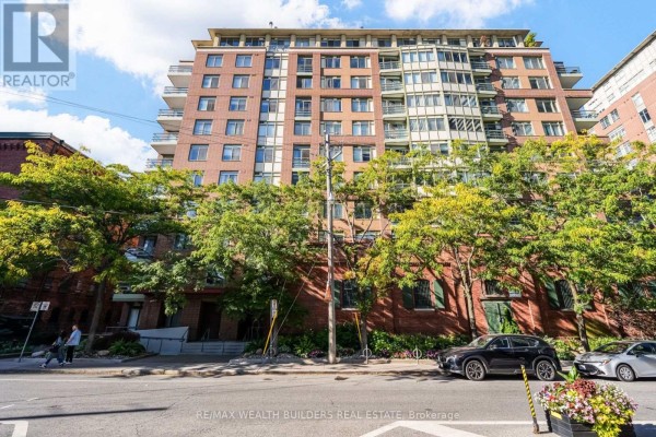 Exterior view of a multi-story brick apartment building with balconies and trees on the street. - Sp09 - 70 Mill Street, Toronto