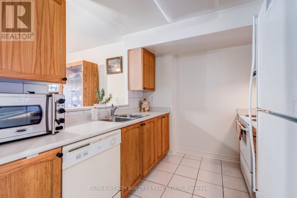 A compact kitchen with light wood cabinets, white countertops, a double sink, and white appliances. - Sp09 - 70 Mill Street, Toronto