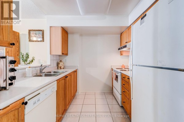 Galley kitchen with light wood cabinets, white tile floor, and white appliances including a refrigerator and stove. - Sp09 - 70 Mill Street, Toronto
