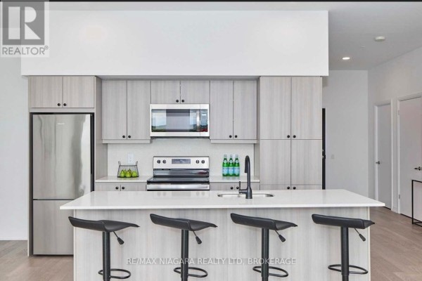 Kitchen island with bar stools, stainless steel refrigerator, microwave, stove, and light wood cabinets. - Sub_penthouse #914 - 7711 Green Vista Gate, Niagara Falls