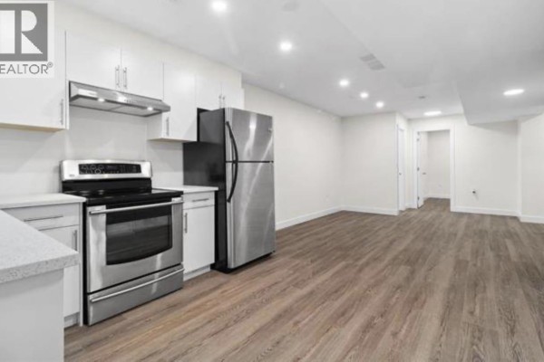 Kitchen with stainless steel appliances, white cabinets, and island, overlooking a living area. - Suite 10321 243 St, Maple Ridge