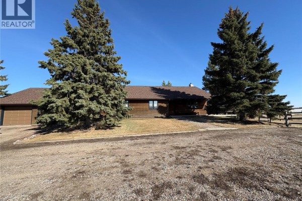 View of the log house exterior with snow on the ground and large evergreen trees. - Tatler Horse Acreage, Leask Rm No  464