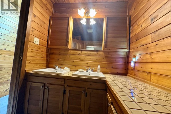 Rear view of the log house with a wooden deck, stone chimney, and satellite dishes. - Tatler Horse Acreage, Leask Rm No  464