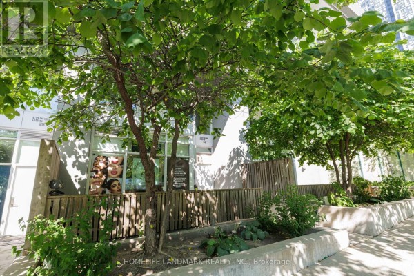 Storefront with wooden fence and green trees in front of a commercial building. - Th02 - 60 Dan Leckie Way, Toronto