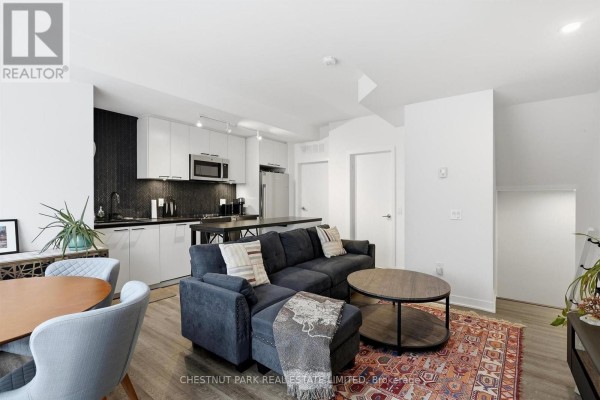 Living room with dark blue sectional sofa, coffee table, and open-concept kitchen. - Th12 - 20 Ed Clark Gardens, Toronto
