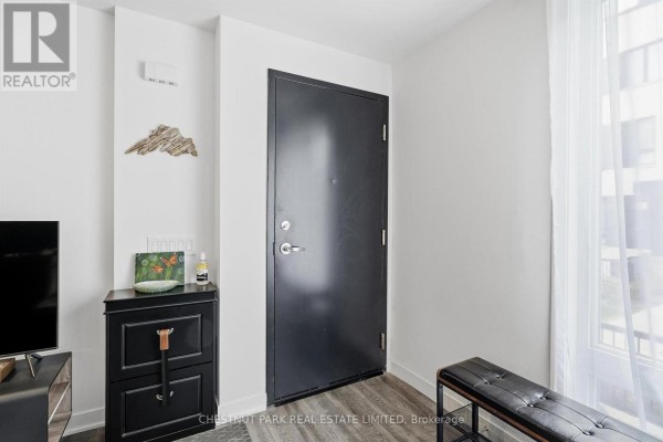 Interior entryway with a black metal door, dark dresser, and bench. - Th12 - 20 Ed Clark Gardens, Toronto