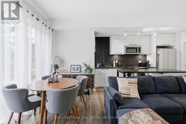 Dining area with oval wood table and grey upholstered chairs, adjacent to kitchen. - Th12 - 20 Ed Clark Gardens, Toronto