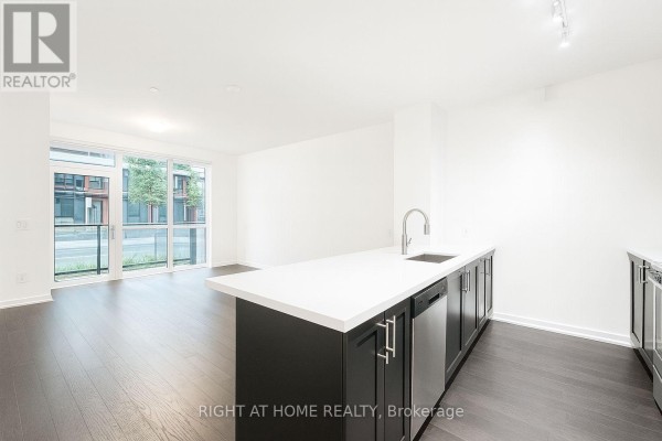 Open concept living area with balcony access, island kitchen, dark wood floors, and white walls. - Th15 - 4055 Parkside Drive, Mississauga