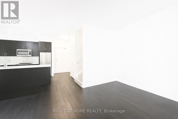 Kitchen area with island, dark cabinets, stainless steel fridge, and view of stairs and white walls. - Th15 - 4055 Parkside Drive, Mississauga