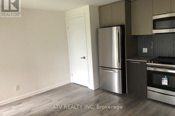 A kitchen area with a refrigerator, dark cabinets, and light grey wood flooring. - Th17 - 10 Brin Drive, Toronto