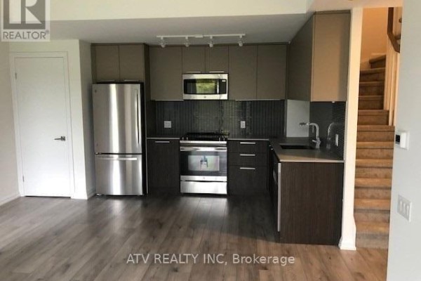 View of a townhouse kitchen with stainless steel appliances and carpeted stairs. - Th17 - 10 Brin Drive, Toronto