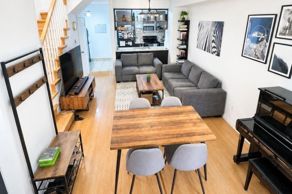 Open concept living and dining area with gray sectional sofa, wooden dining table, and stairs. - Th25 - 290 Village Green Square, Toronto