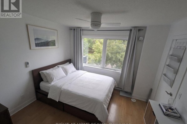 Bedroom with a queen-size bed, white linens, large window with gray curtains, and wooden floor. - Th25 - 290 Village Green Square, Toronto