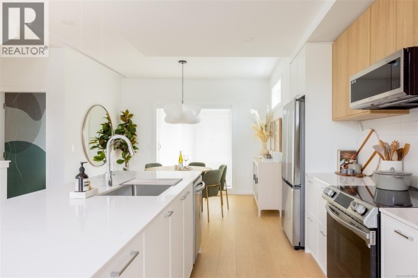 Kitchen with island, stainless steel refrigerator, dining table with chairs, and large mirror on wall. - Th6 3450 Whittier Ave, Saanich