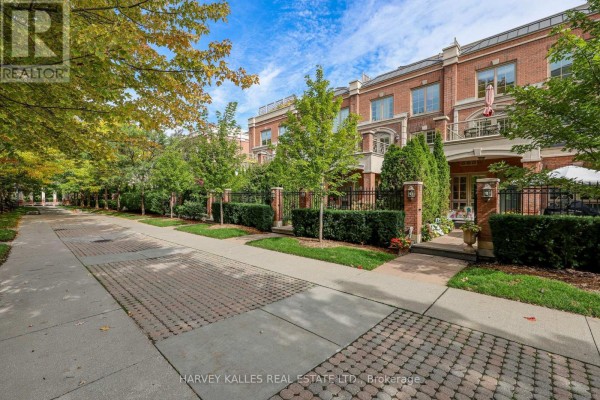 Street view of brick townhouses with paved walkways and mature trees. - Th9 - 21 Burkebrook Place, Toronto