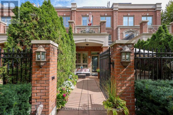Close-up of townhouse entrance with brick pillars, black fence, and flowers. - Th9 - 21 Burkebrook Place, Toronto