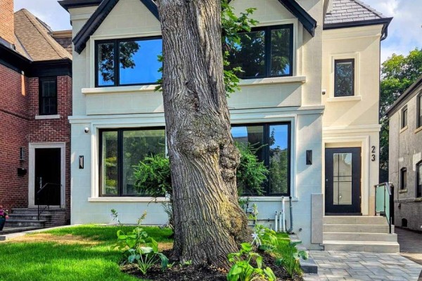 Front exterior of a multi-family home with a large tree, green lawn, and modern windows. - The Palazzo - 23 Coulson Avenue, Toronto