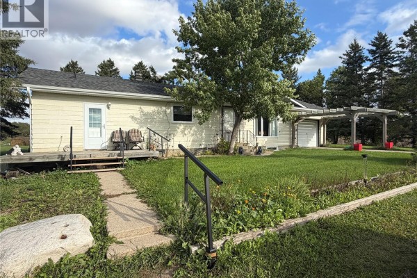 Side view of a beige house with a wooden deck and mature trees in the yard. - Thiessen Acreage, Laird Rm No  404