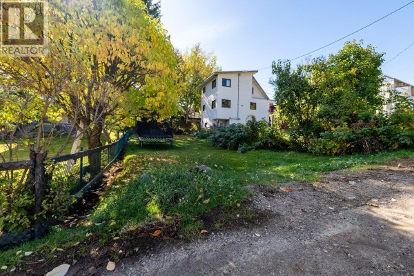 A view of a yard with trees, a trampoline, and a white house. - Third Avenue Lot# Lot 7, Rossland