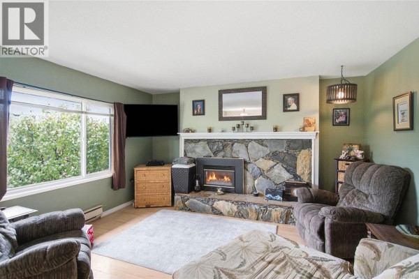 Living room with a stone fireplace, television, and large window with green foliage view. - Trunk Rd 7 Trunk Rd, Duncan