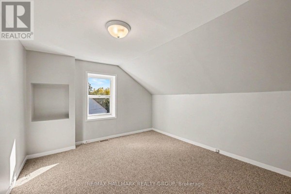 Carpeted room with light gray walls, sloped ceiling, and a single window with a view of trees. - Unit 1 - 216 Bell Street, Arnprior
