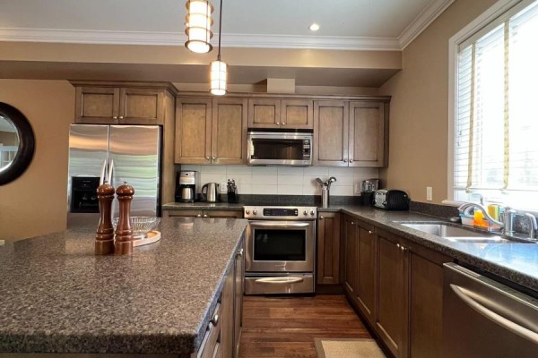 A kitchen with granite countertops, stainless steel appliances, and dark wood cabinets. - Unit 11 - 301 Emerald Hills Court, Seguin