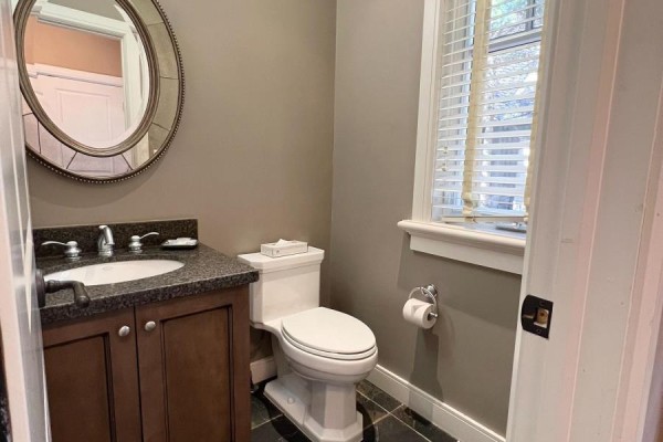 A powder room with a dark granite countertop, dark wood vanity, and a decorative mirror. - Unit 11 - 301 Emerald Hills Court, Seguin