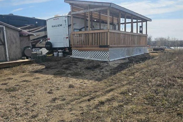 Paved patio with Adirondack chairs and a stone fire pit, overlooking a field and trees. - Unit 118, 65275 Range Road 114a, Lac La Biche