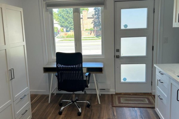 Interior view of a studio with a desk and chair, large window, and a white wardrobe with storage drawers. - Unit 2 - 1473 Adelaide Street N, London North
