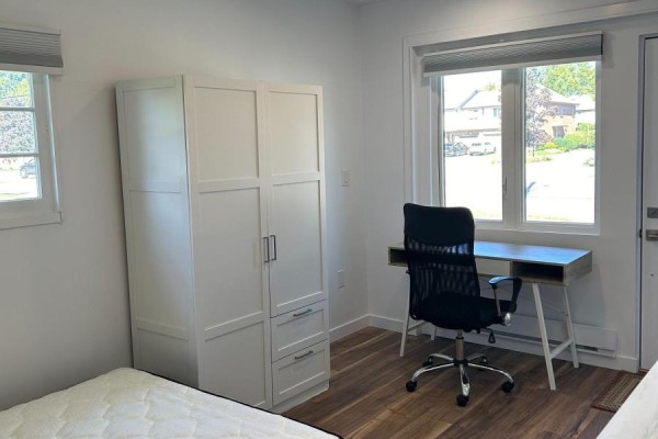 Studio layout featuring a white wardrobe, desk, chair, and a window looking out onto a residential street. - Unit 2 - 1473 Adelaide Street N, London North