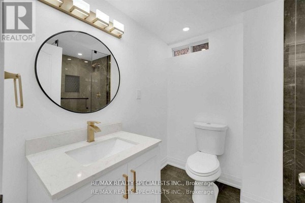 Bathroom vanity with white countertop, gold faucet, and round mirror. - Unit 2 - 7294 Rosehurst Drive, Mississauga