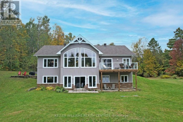 Rear view of a two-story grey house with a large arched window, balcony, and walkout basement. - Unit 4 - 1623 Houseys Rapids Road, Gravenhurst
