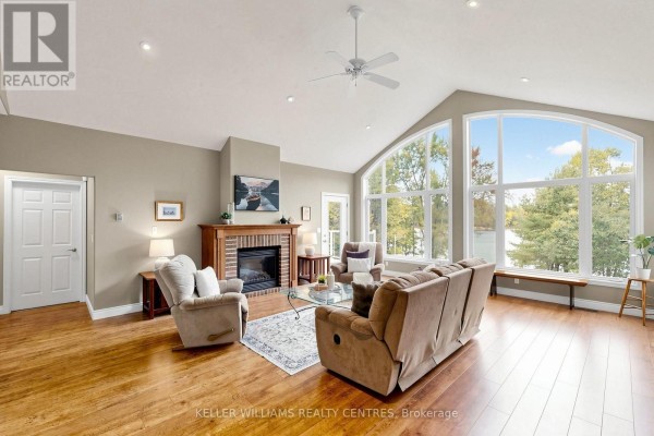 Living room with vaulted ceiling, fireplace, large windows, and hardwood floors. - Unit 4 - 1623 Houseys Rapids Road, Gravenhurst