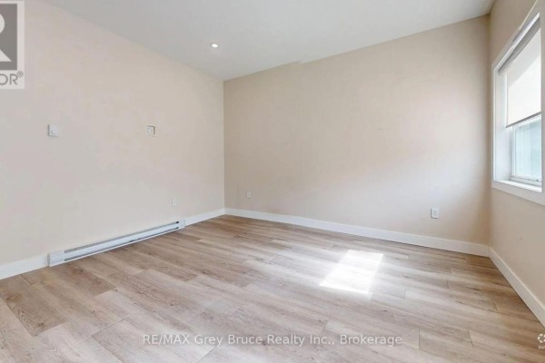 Empty room with beige walls, light wood-look flooring, baseboard heating, and a single window. - Unit 4 - 39 1st Avenue S, Arran Elderslie