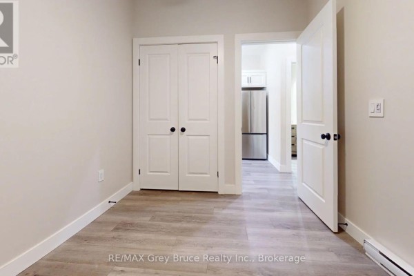 Interior view showing double closet doors, an open doorway revealing a kitchen with a stainless steel refrigerator. - Unit 4 - 39 1st Avenue S, Arran Elderslie